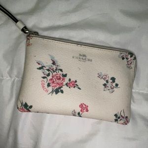 A coach wallet, white, with pink flowers, has two pockets inside.